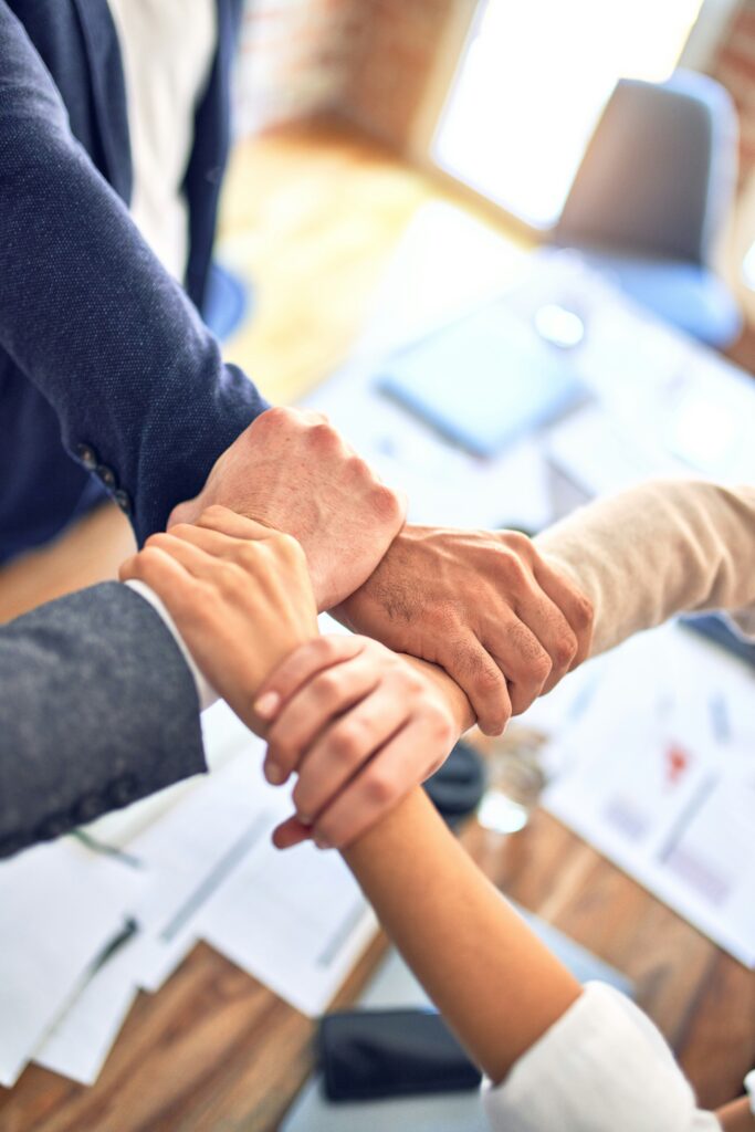 A close-up image of 4 people whose arms are interlocked to give an impression of teamwork.